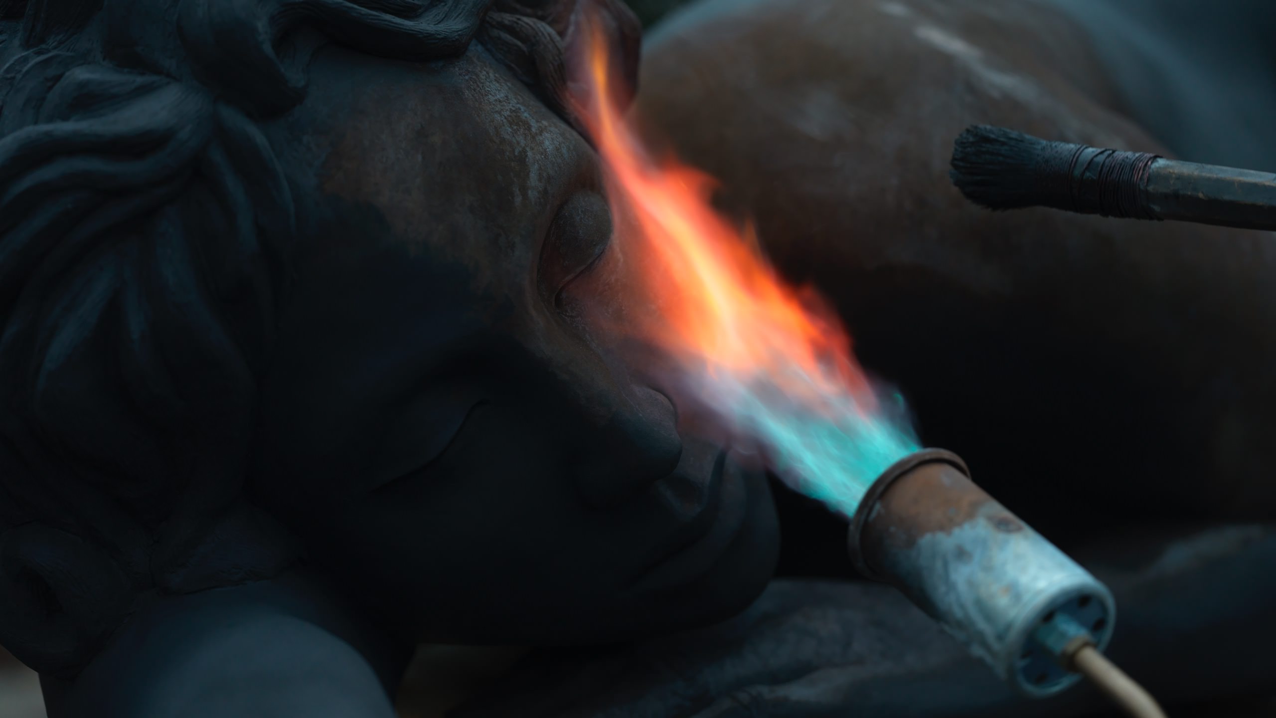 Helga Vockenhuber Patinating Apatheia with FireArtist Helga Vockenhuber is shown working on her bronze sculpture Apatheia, applying patina with fire. The open flame transforms the surface of the sculpture, creating dark, earthy, and golden tones. The imag Helga Vockenhuber uses an open flame to patinate her bronze sculpture Apatheia, creating warm tones and surface variations on the artwork.
